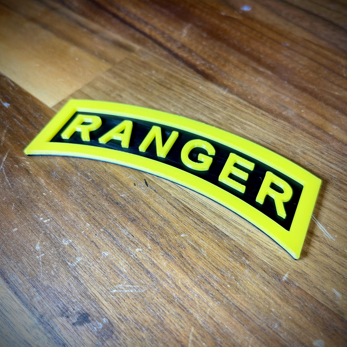 3D Army Ranger tab replica showcasing the iconic yellow-on-black design on a wooden surface.