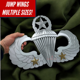 Hand holding a shiny parachutist jump wings badge against a green background, showcasing multiple sizes available.