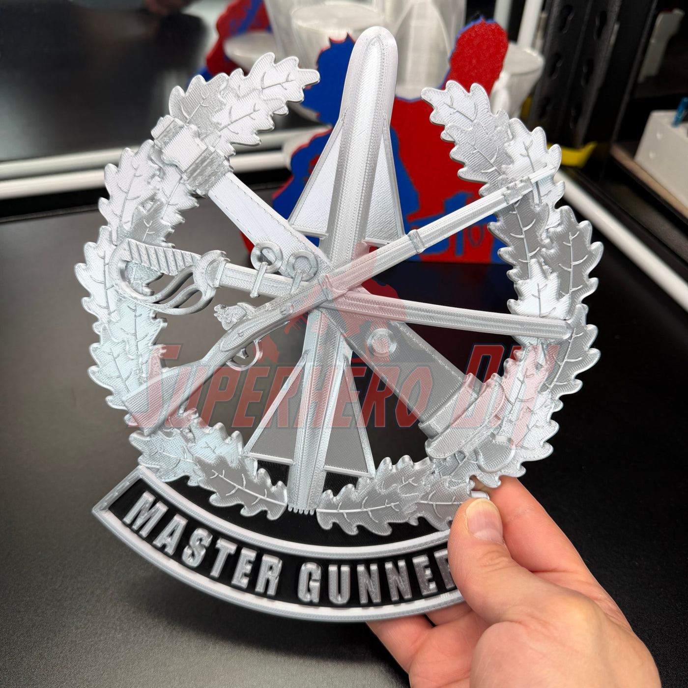 Master Gunner Badge display insignia held in hand, showcasing intricate 3D design and details.