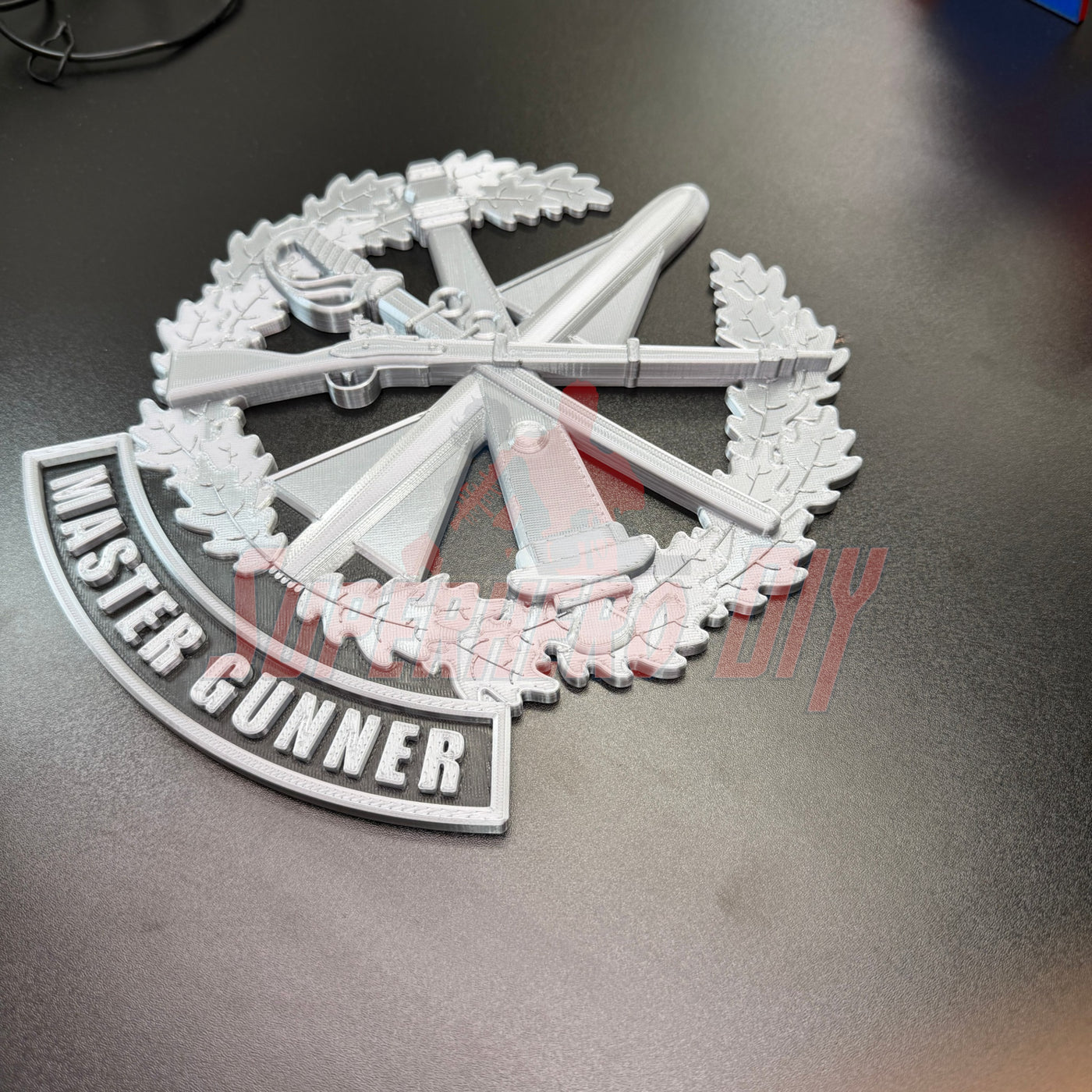 3D Master Gunner Badge display insignia on a dark surface, showcasing military arms and the title 'MASTER GUNNER'.