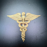 Gold army medical corps caduceus wall display with wings and serpents on dark background.