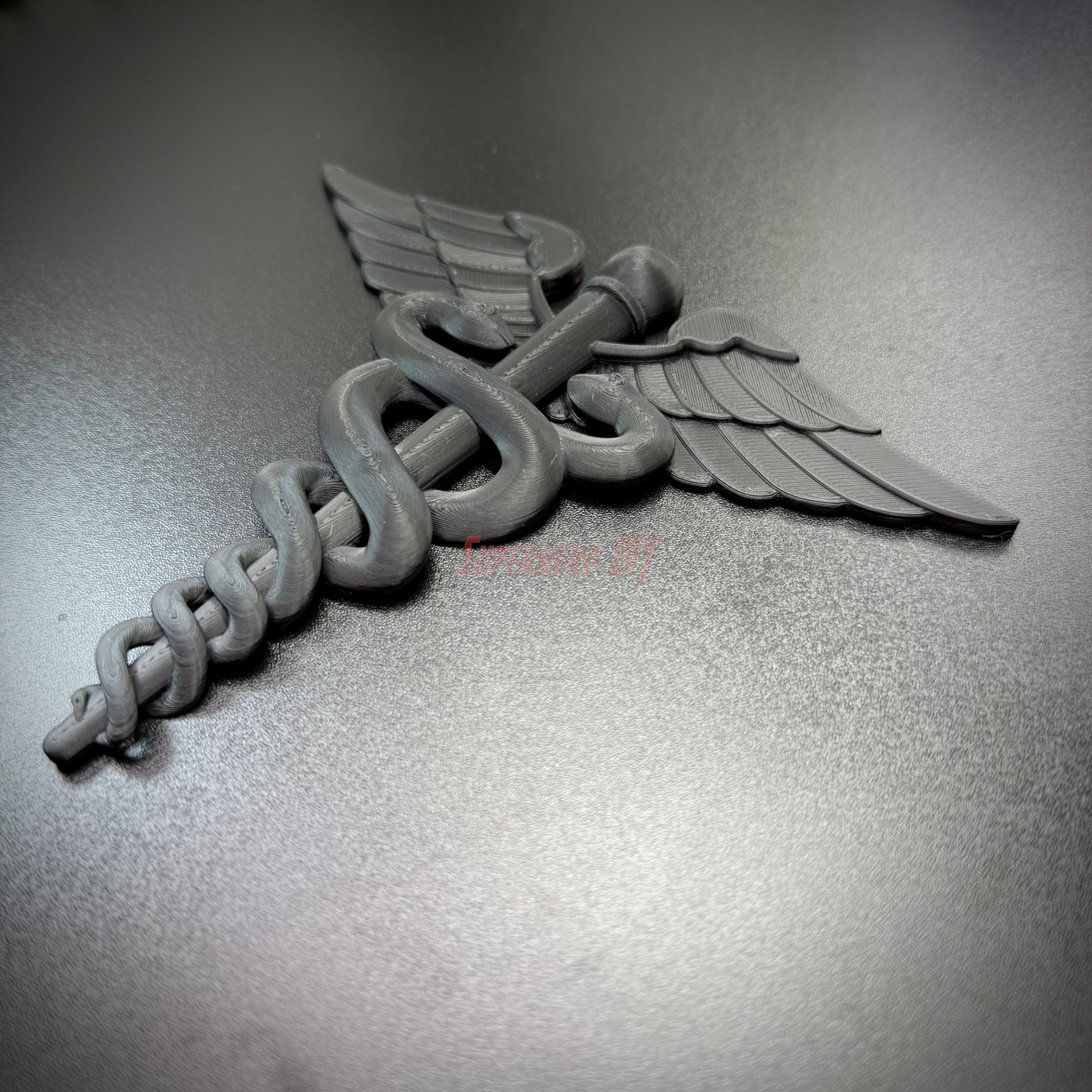 Army Medical Corps caduceus wall display in black, featuring entwined serpents and wings on a flat background.