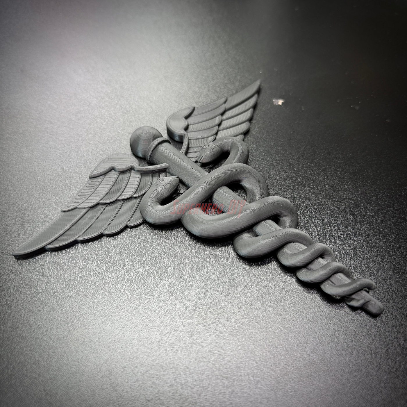 Army medical corps caduceus wall display in black, featuring twin serpents and wings on a sleek surface.