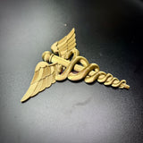 army medical corps caduceus wall display in gold, featuring twin serpents and wings on a flat surface.