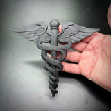 Army Medical Corps Caduceus wall display held in hand, showcasing intricate wings and serpents in black finish.