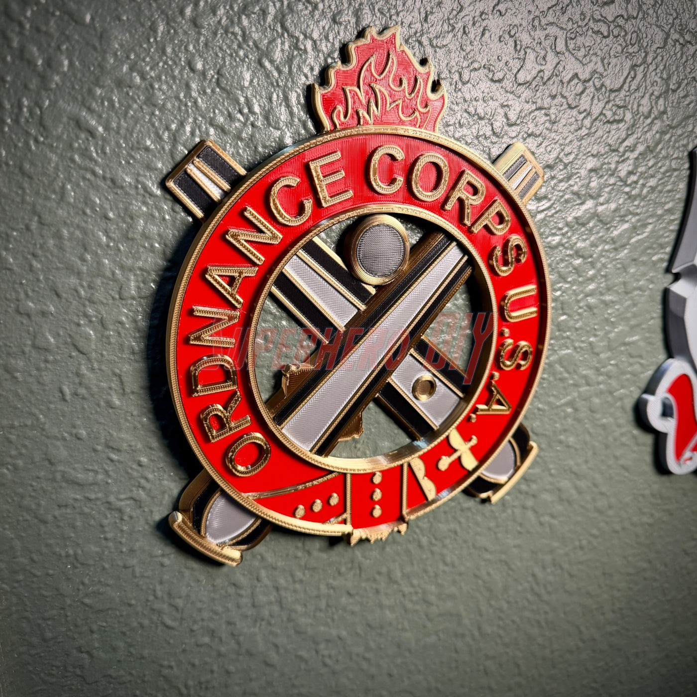 Ordnance regimental crest displayed as a decorative plaque in vibrant red and gold on a wall.