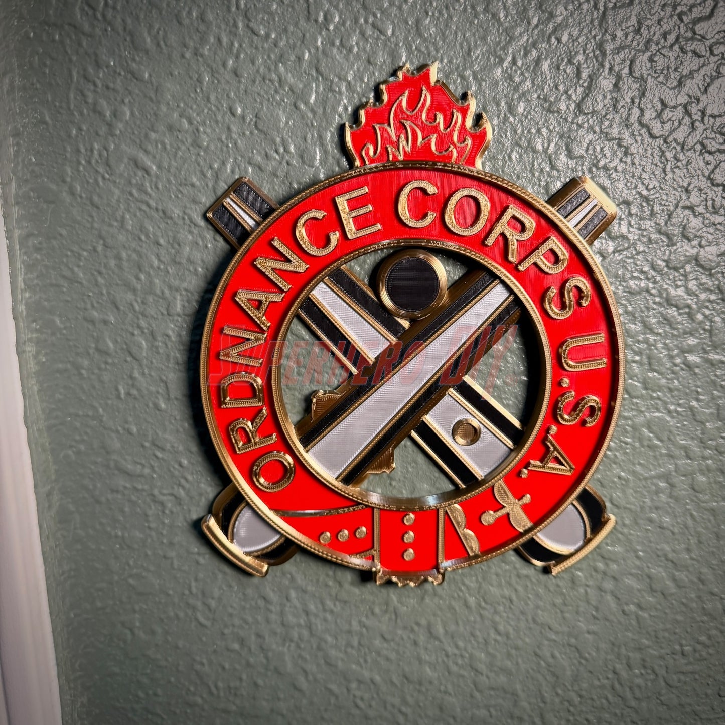 Ordnance Regimental Crest displayed on a wall, featuring red and gold colors and symbols of the Ordnance Corps, USA.