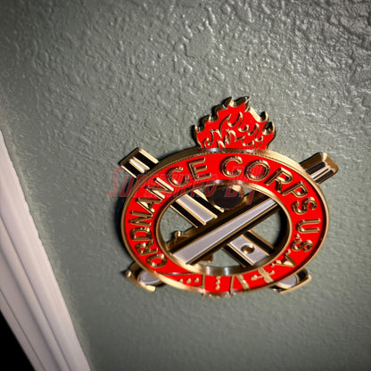 Ordnance Regimental Crest displayed on a wall, symbolizing the Ordnance Corps with red and gold colors.