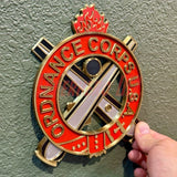 Ordnance Regimental Crest displayed on a wall, featuring red and gold colors, representing the Ordnance Corps.