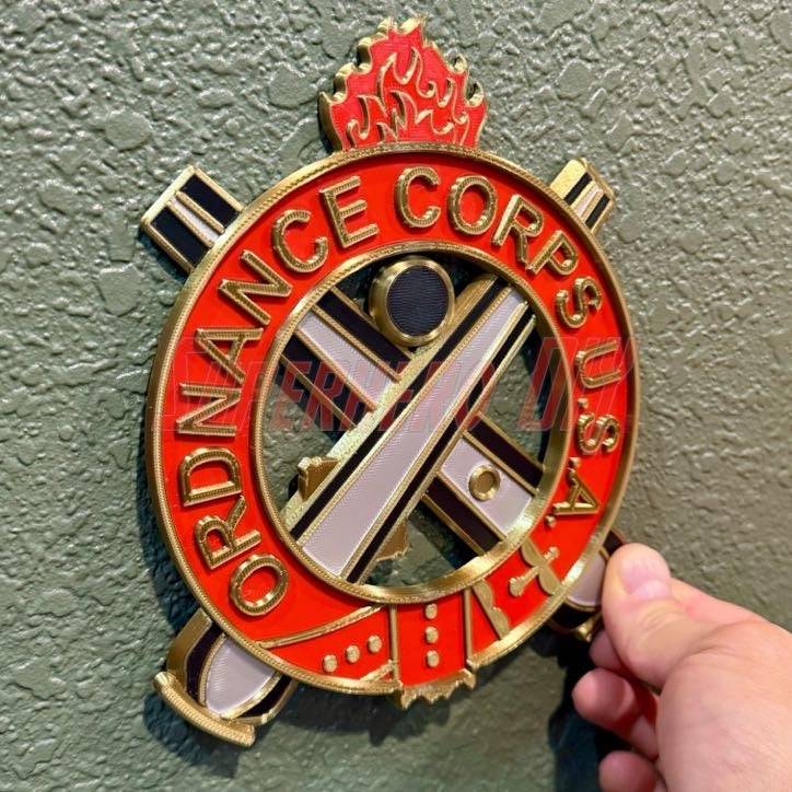 Ordnance Regimental Crest displayed on a wall, featuring red and gold colors, representing the Ordnance Corps.