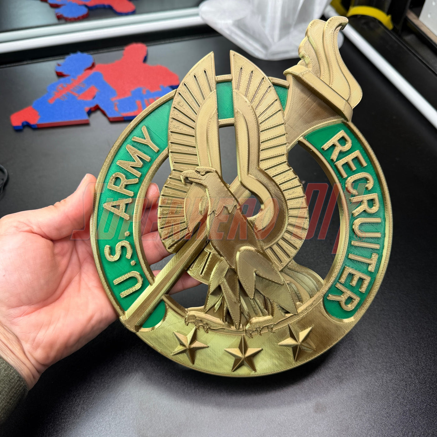 Hand holding an Army Recruiter Badge insignia with eagle and stars, showcasing the U.S. Army Recruiter emblem.