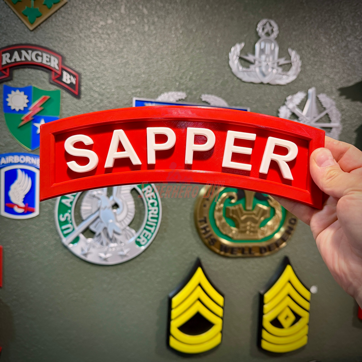 3D sapper tab held in hand, showcased with military insignia in the background.