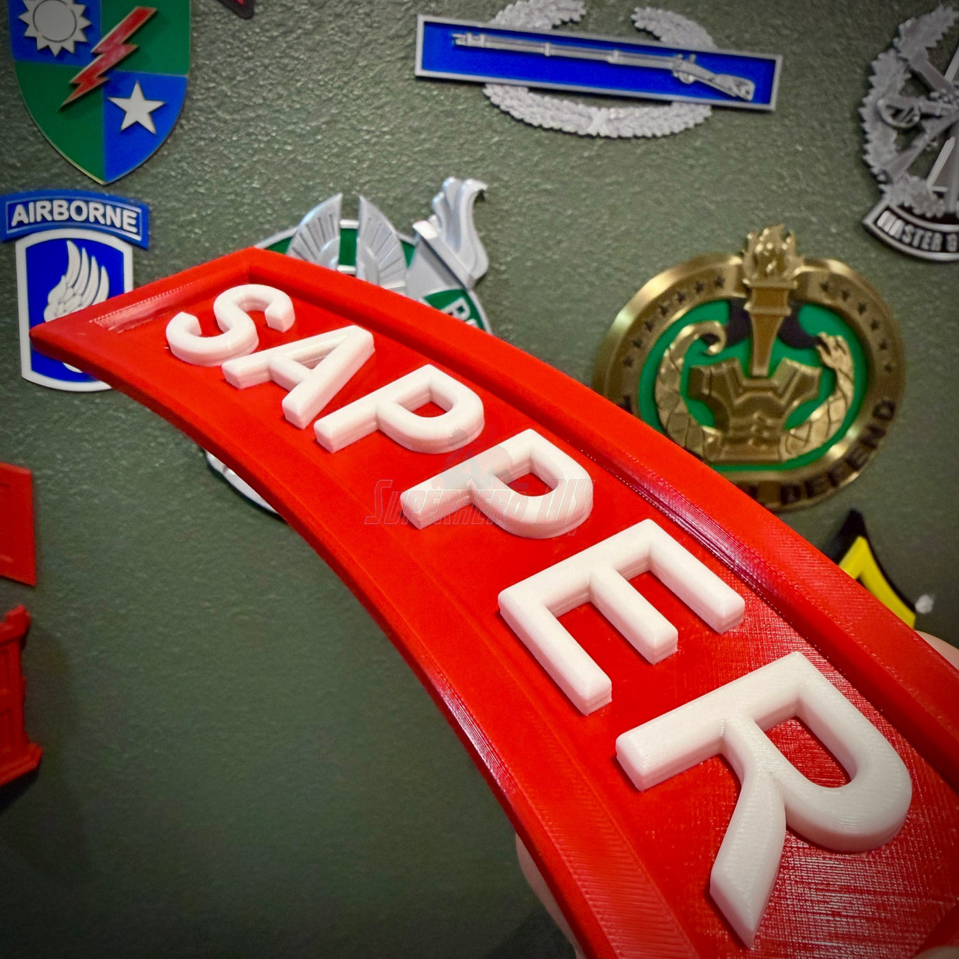 3D sapper tab display piece showcasing the word SAPPER in raised white letters on a red background.