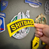 Person holding a SHITBAG tab in yellow and black, perfect gag gift for military friends.