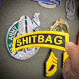 Image of a hand holding the SHITBAG tab, a gag gift in a classic Army style, perfect for roasting your battle buddy.