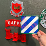 3D-printed 3rd Infantry Division display insignia in bold blue-and-white pattern held against military wall decor.