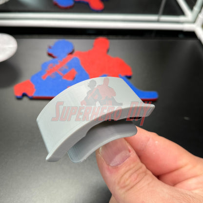 Gray hat display wall mount held in hand, showcasing design with superhero silhouette in the background.