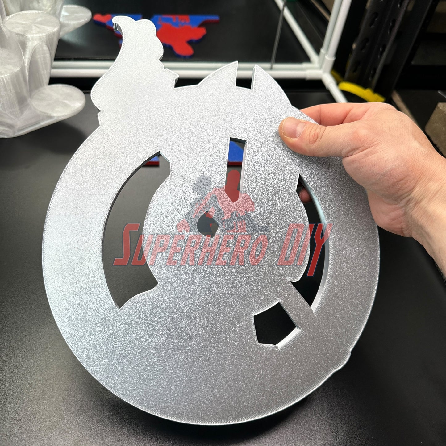 Person holding a metallic superhero logo cutout for wall display.