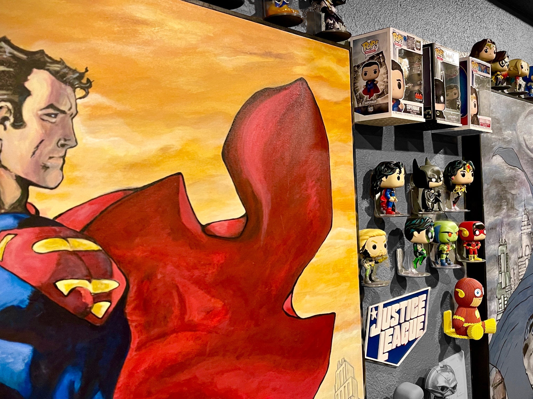 Superhero collectibles like funko pops and action figures displayed on a gray wall