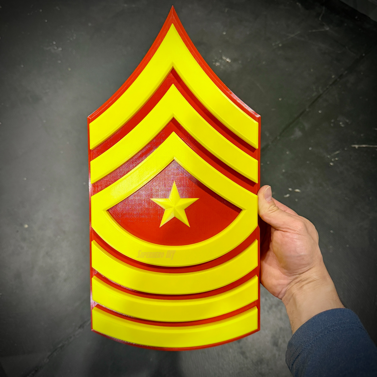 USMC Sergeant Major (E-9) rank insignia held in hand over a dark concrete background, star centered