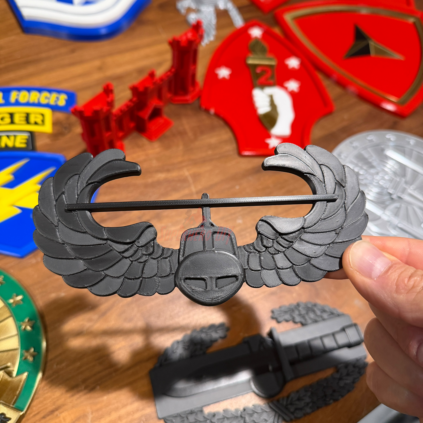 Air Assault Badge display held by hand among various military insignia on a wooden surface.