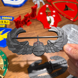 Air Assault Badge display held by hand among various military insignia on a wooden surface.