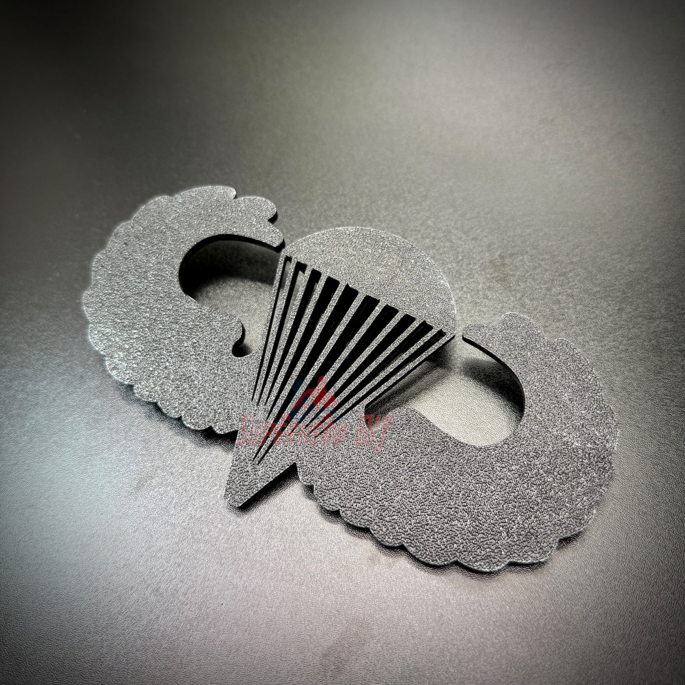 Subdued airborne jump wings replica badge displayed on a dark surface, showcasing detailed design and craftsmanship.