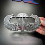 Subdued airborne jump wings replica badge, showcasing detailed design of parachute and wings.