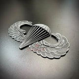 Subdued airborne jump wings replica badge with parachute design on a dark background