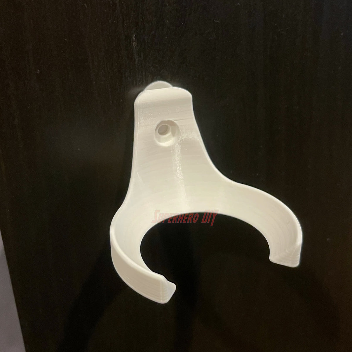 Empty white baseball holder wall mount on a dark wall, screw hole visible