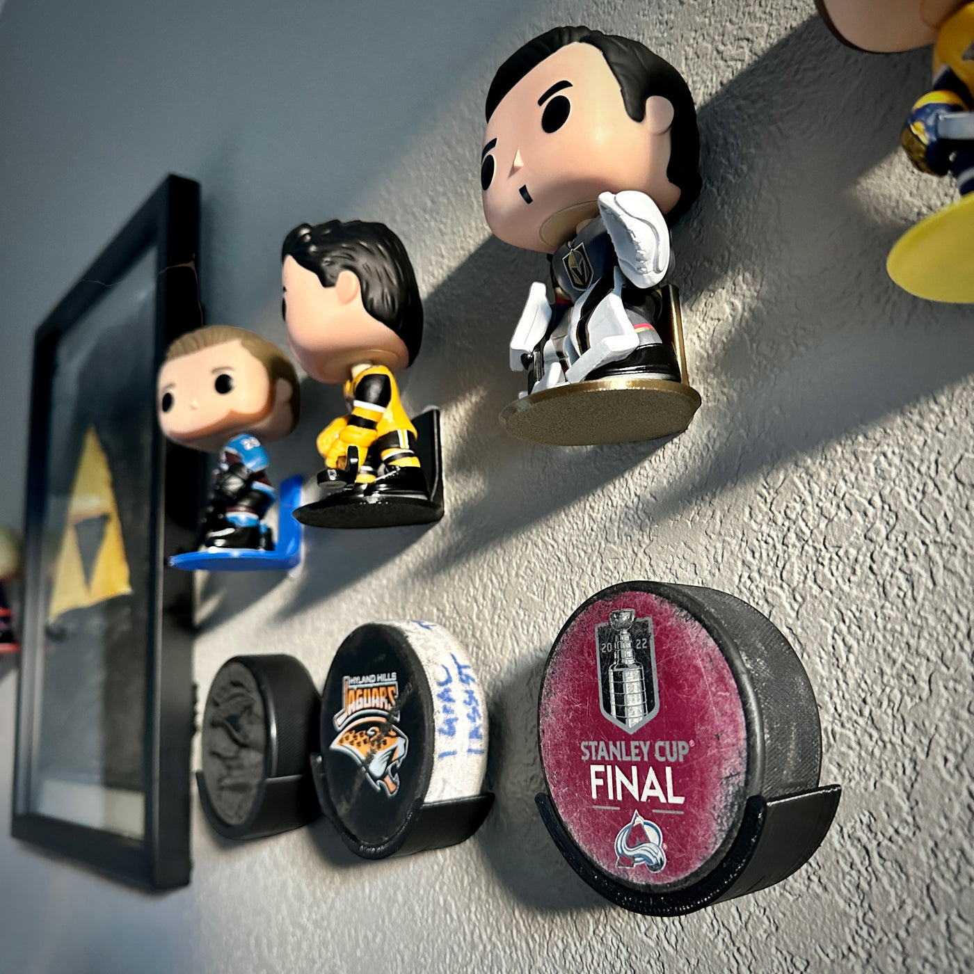 Hockey puck holder showcasing pucks including Stanley Cup Final on a wall with funko pop figures.