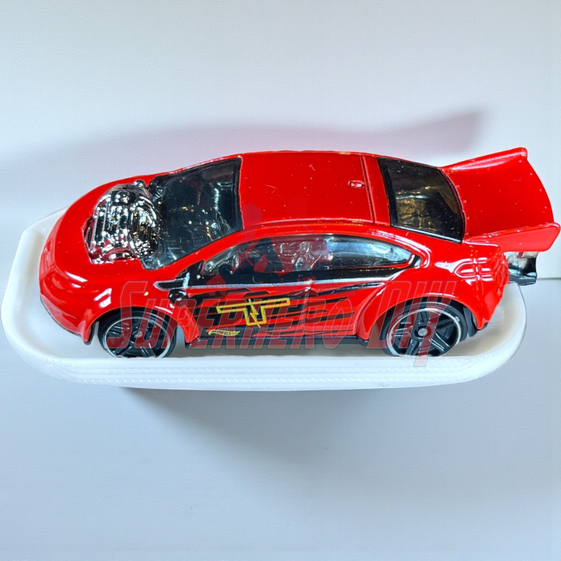 Red diecast car on display shelf for Hot Wheels, featuring smooth, curved surface for 1:64 model cars. Command strip included for mounting.
