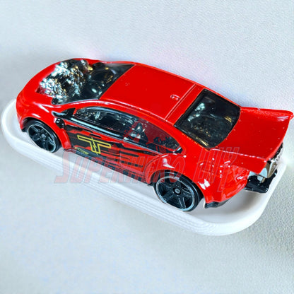 Red 1:64 diecast car displayed on a white display shelf for Hot Wheels, showcasing sleek design with curved surface.
