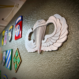 parachutist jump wings badge displayed on a wall with various military insignias behind it