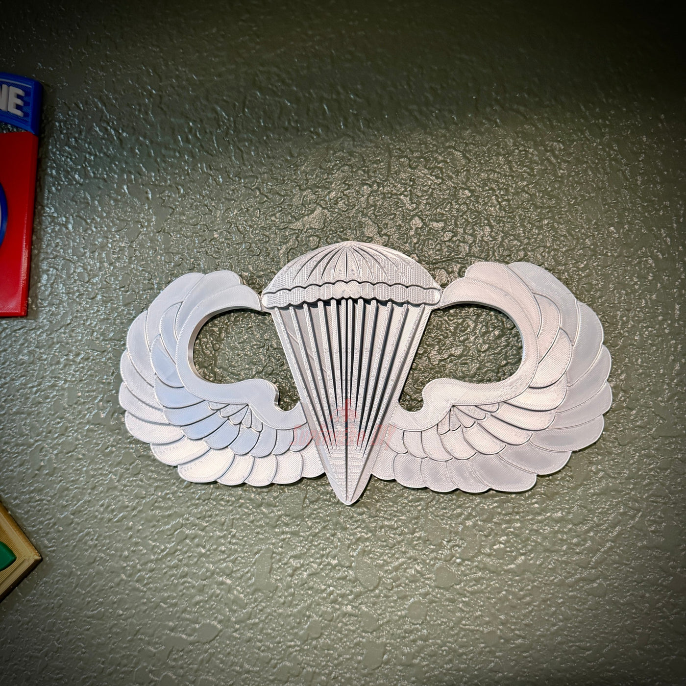 Parachutist jump wings badge with wings and parachute design displayed on a wall.