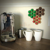 Honeycomb wall mount for original Nespresso coffee pod organizer holding multiple capsules beside a coffee machine.
