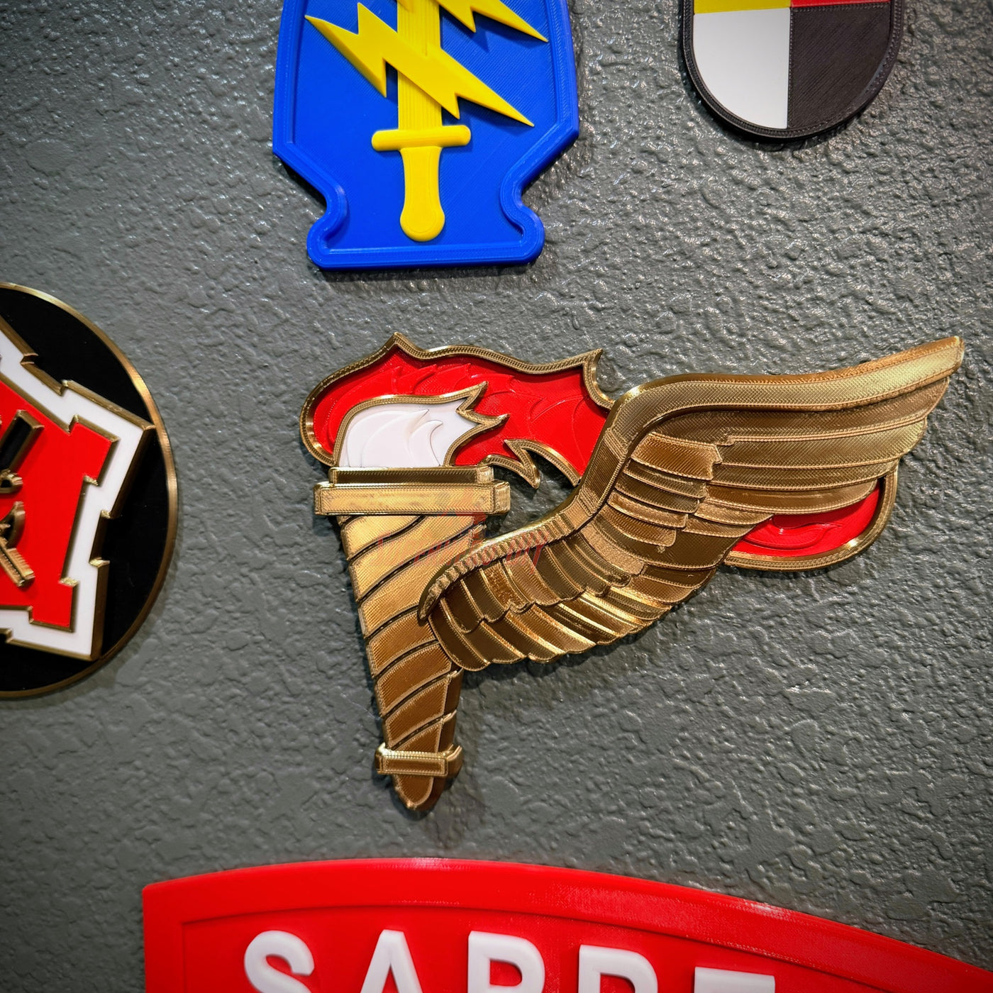 Army Pathfinder Badge with winged torch design, showcased among various military insignia on a display wall.
