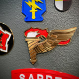 Army Pathfinder Badge with winged torch design, showcased among various military insignia on a display wall.