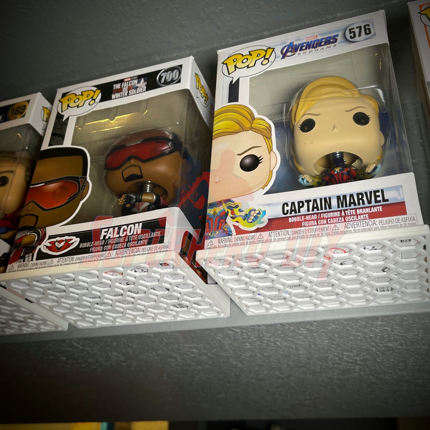 Hexagon Funko Pop display shelves holding Falcon and Captain Marvel figures in protector cases.