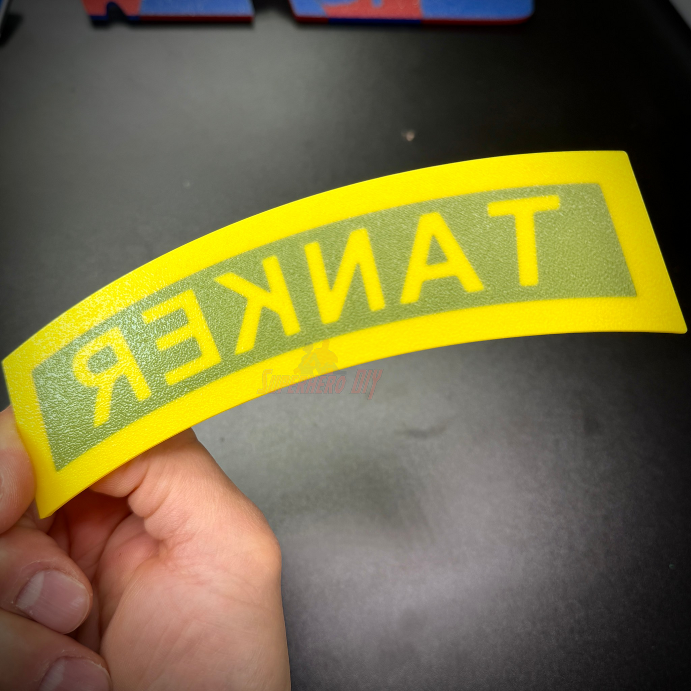 3D tanker tab displayed in yellow with raised lettering, showcasing the word 'TANKER' for military use.
