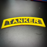 3D tanker tab in bright yellow with raised lettering displayed on a black surface.