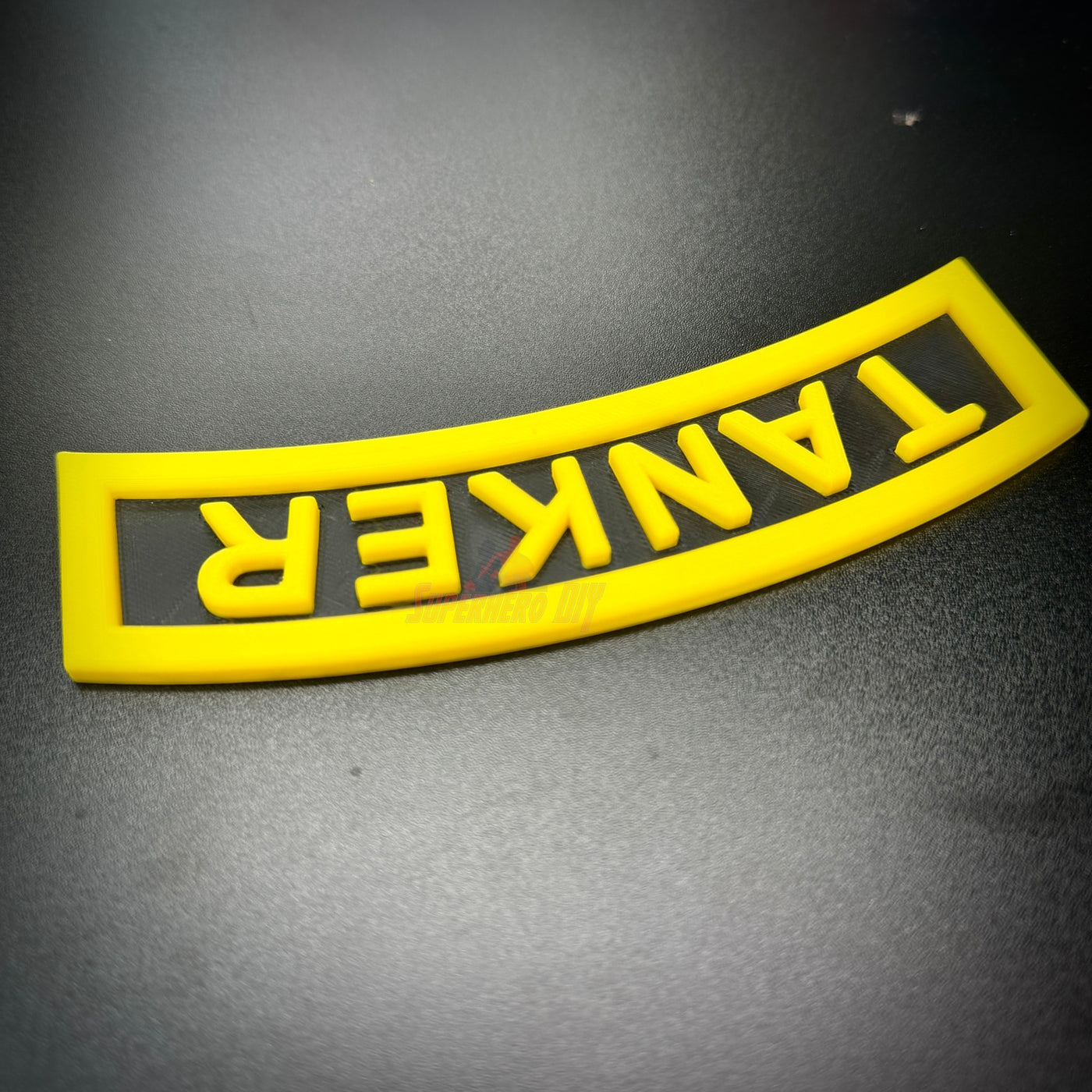 3D tanker tab in bright yellow, showcasing raised lettering and an arch design on a black background.