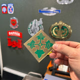 Hand holding 4th Infantry Division display insignia against a backdrop of military patches.