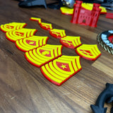Detailed USMC enlisted rank insignia displayed on a wooden table, showcasing multiple 3D-printed ranks in red and yellow.