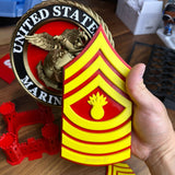 USMC enlisted rank insignia in red and yellow held by a hand, showcasing Marine Corps pride.