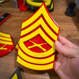 Hand holding a red and yellow USMC enlisted rank insignia, showcasing detailed 3D printing for Marine Corps pride.