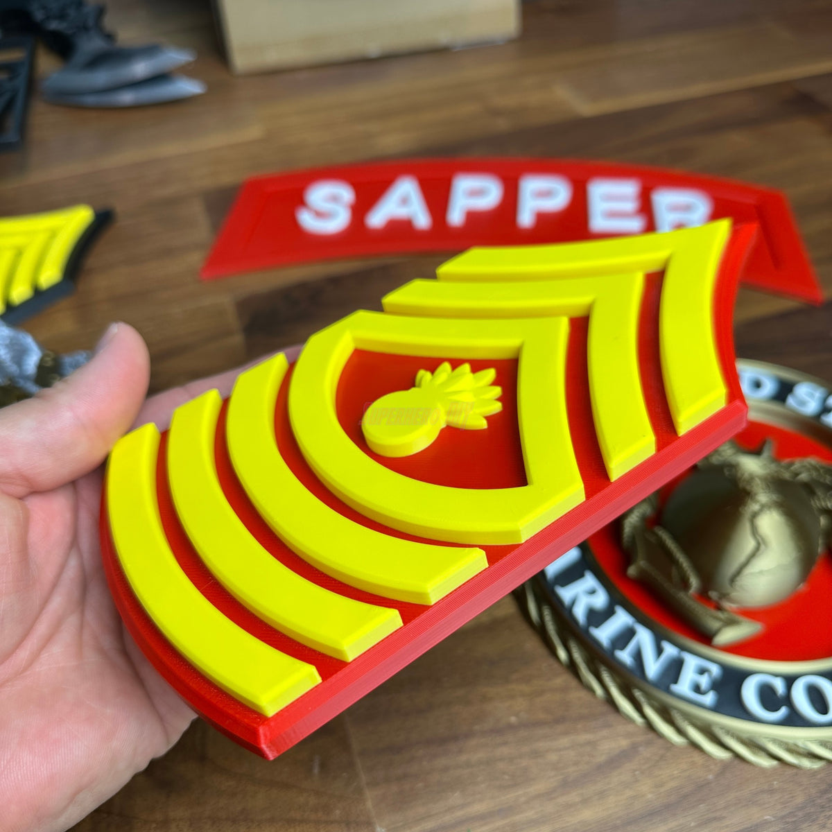 USMC enlisted rank insignia in yellow and red for Master Gunnery Sergeant, representing Marine Corps NCO rank with detail.