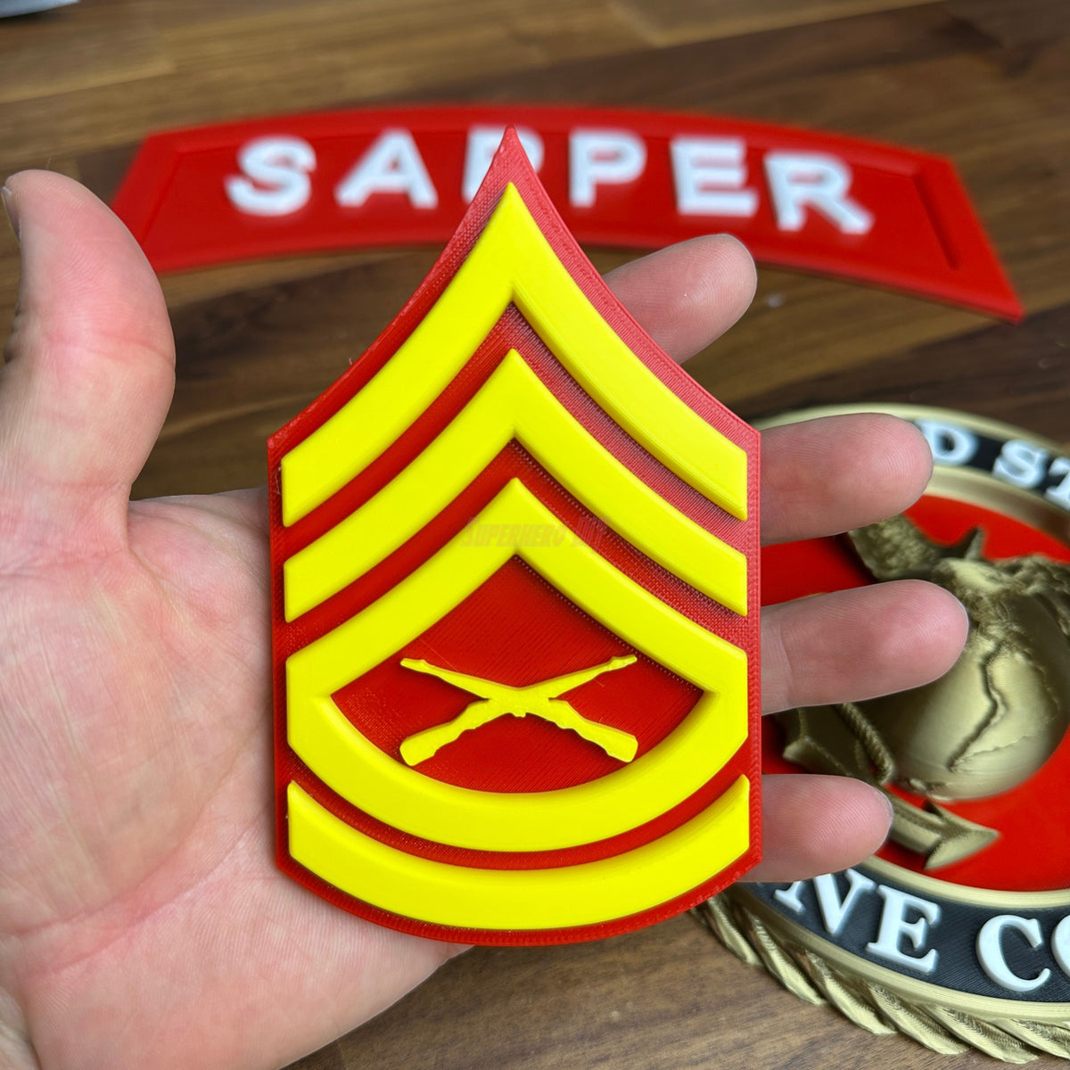 USMC enlisted rank insignia in hand, featuring Gunnery Sergeant rank in red and yellow design with crossed rifles.