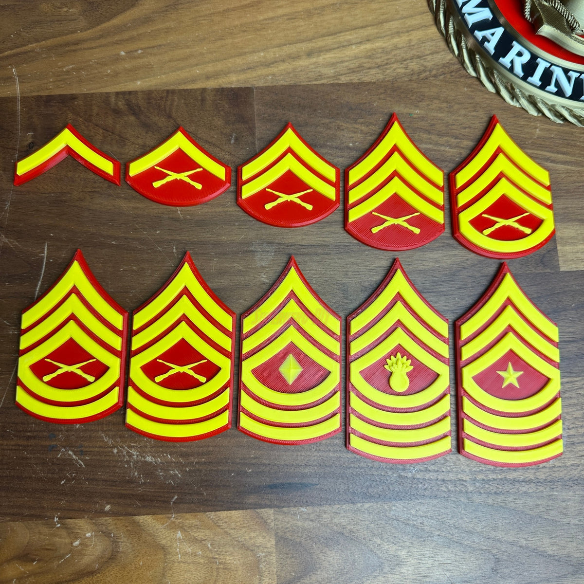 USMC enlisted rank insignias displayed on a wooden surface, featuring red and yellow designs for Marine Corps ranks.